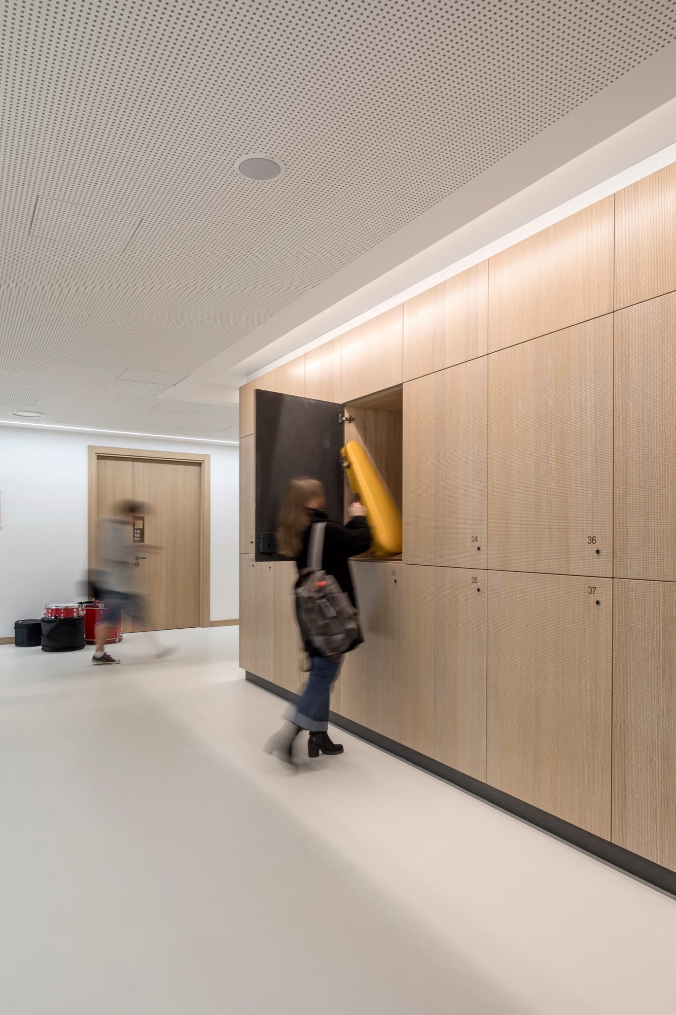 Instrument lockers in micro-perforated timber lining a school corridor